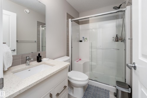 Modern bathroom featuring a glass-enclosed shower with a built-in bench, a single vanity with a solid surface countertop, and a large wall-mounted mirror - 2520 152 Avenue, Edmonton, AB 