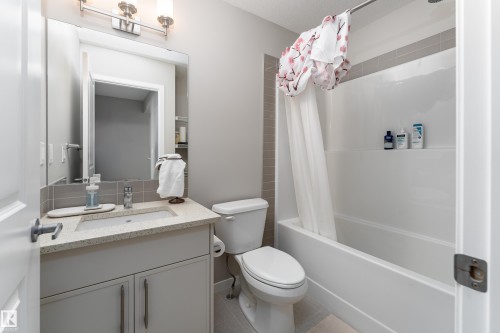 Bathroom featuring a white bathtub with a tiled surround, a toilet, and a vanity with an integrated sink and light-colored countertop - 2520 152 Avenue, Edmonton, AB 
