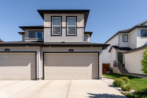 Modern exterior featuring light-colored siding with dark trim accents, a prominent upper-level window array, and two attached garages with panel doors - 2520 152 Avenue, Edmonton, AB 