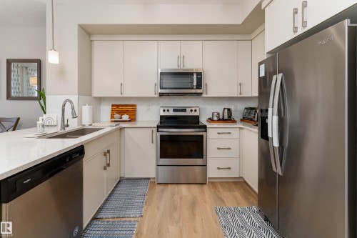 Modern kitchen featuring light cabinetry, stainless steel appliances, a white tile backsplash, light wood-finish laminate flooring, and quartz countertop. - 2520 152 Avenue, Edmonton, AB 