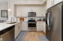 Modern kitchen featuring light cabinetry, stainless steel appliances, a white tile backsplash, light wood-finish laminate flooring, and quartz countertop. - 2520 152 Avenue, Edmonton, AB 