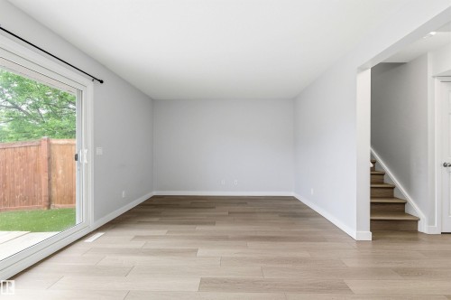 Spacious interior featuring wood-finish flooring, white baseboards, and light gray walls - 18353 66 Avenue, Edmonton, AB 