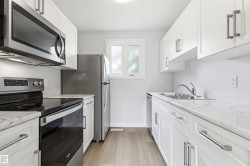 Bright kitchen featuring white cabinetry with brushed nickel hardware, stainless steel appliances, marble-look countertops, and wood-finish flooring - 