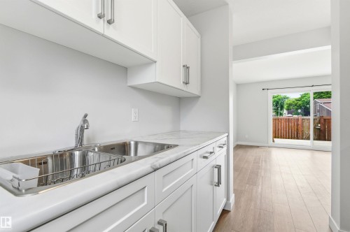 Kitchenette featuring white cabinetry with brushed nickel hardware, a stainless steel double basin sink, and white countertops - 18353 66 Avenue, Edmonton, AB 