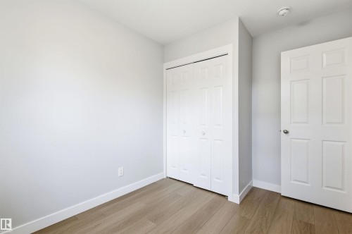 Room featuring light wood-finish flooring, white baseboards, a white six-panel door, and a white bi-fold closet door - 18353 66 Avenue, Edmonton, AB 