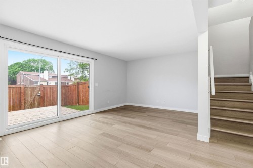 Spacious main living area featuring light wood-finish flooring, neutral paint, a large glass sliding door, and a staircase with contemporary railing - 18353 66 Avenue, Edmonton, AB 