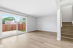 Spacious main living area featuring light wood-finish flooring, neutral paint, a large glass sliding door, and a staircase with contemporary railing - 
