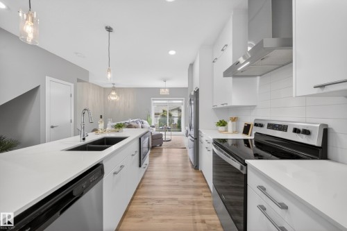 Contemporary kitchen featuring a large island with an undermount sink, a stainless steel appliance suite, white cabinetry, and wood-finish flooring - 52 1729 Keene Crescent, Edmonton, AB 