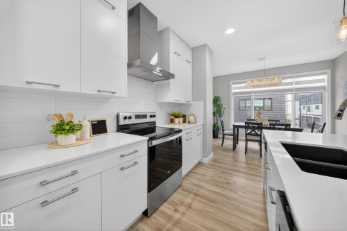 Modern kitchen featuring stainless steel appliances, white cabinetry with brushed nickel hardware, light-colored countertops, and wood-finish flooring - 52 1729 Keene Crescent, Edmonton, AB 