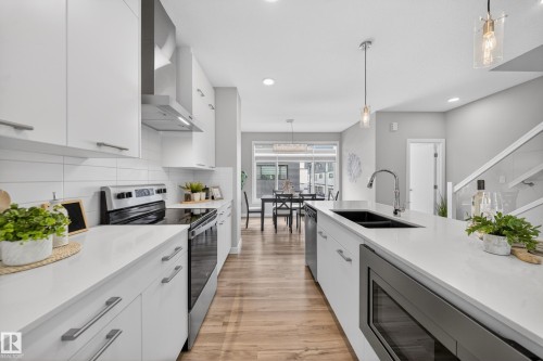 Modern kitchen featuring white cabinetry, light countertops, wood-finish flooring, a stainless steel appliance suite, and an integrated microwave - 52 1729 Keene Crescent, Edmonton, AB 