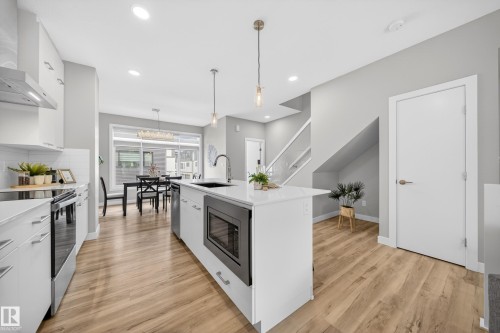 Contemporary kitchen featuring a white island with an undermount sink and integrated microwave, stainless steel appliances, and light wood-finish flooring - 52 1729 Keene Crescent, Edmonton, AB 
