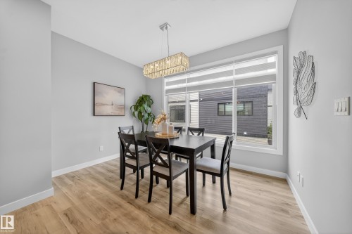Bright dining area featuring wood-finish flooring, a large window with privacy blinds, and a contemporary chandelier - 52 1729 Keene Crescent, Edmonton, AB 