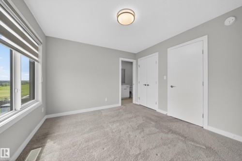 Carpeted room featuring a large window with blinds, a flush-mount ceiling light, and two white panel doors - 52 1729 Keene Crescent, Edmonton, AB 