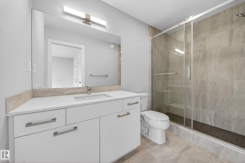 Bathroom featuring a white vanity with an integrated sink, a large wall-mounted mirror, and contemporary lighting - 52 1729 Keene Crescent, Edmonton, AB 
