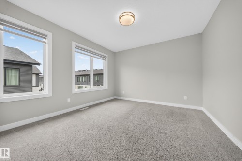 Bright room featuring neutral gray walls, plush gray carpeting, and two large windows with white trim - 52 1729 Keene Crescent, Edmonton, AB 