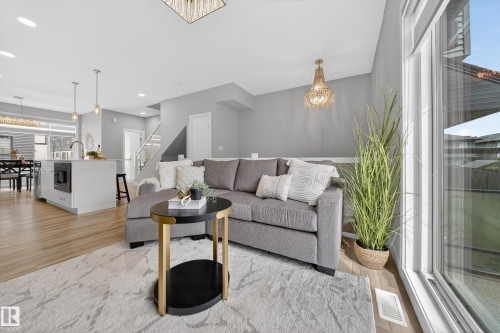 Open-concept living area featuring wood-finish flooring, a large window, a crystal chandelier, a kitchen island with a built-in microwave, and a dining area with a modern linear chandelier - 52 1729 Keene Crescent, Edmonton, AB 