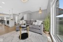 Open-concept living area featuring wood-finish flooring, a large window, a crystal chandelier, a kitchen island with a built-in microwave, and a dining area with a modern linear chandelier - 52 1729 Keene Crescent, Edmonton, AB 