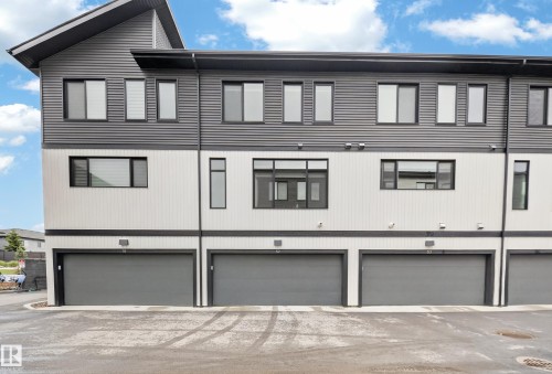 Modern townhome exterior featuring a striking two-tone facade with dark grey corrugated siding and light vertical paneling - 52 1729 Keene Crescent, Edmonton, AB 