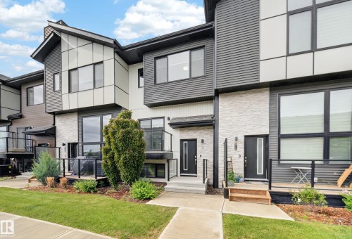 Modern multi-level exterior featuring varied siding materials, large windows, a front porch, a ground-level patio, and an established lawn with landscaping - 52 1729 Keene Crescent, Edmonton, AB 
