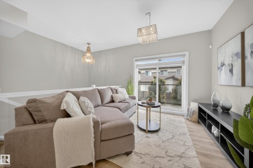 Light-filled living area featuring wood-finish flooring, a contemporary chandelier, and direct access to a balcony with glass railings - 52 1729 Keene Crescent, Edmonton, AB 