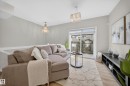 Light-filled living area featuring wood-finish flooring, a contemporary chandelier, and direct access to a balcony with glass railings - 52 1729 Keene Crescent, Edmonton, AB 