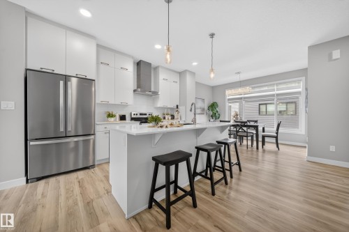 Open-concept kitchen with wood-finish flooring, white cabinetry, stainless steel appliances, and a central island with countertop seating - 52 1729 Keene Crescent, Edmonton, AB 