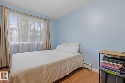 Bedroom featuring wood-finish flooring, light blue walls, and a large window with sheer and blackout curtain rods - 