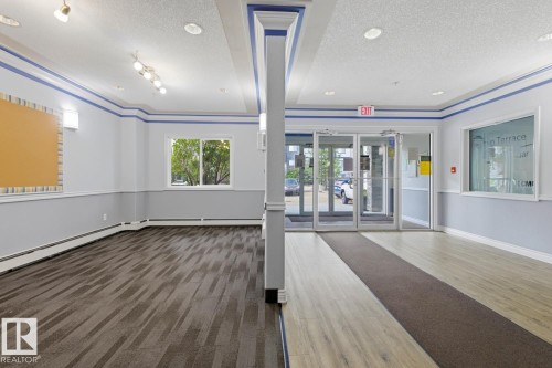 Spacious common area featuring a mix of wood-finish flooring and patterned carpet - 211 1204 156 Street Nw, Edmonton, AB 