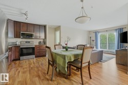 Open-concept living area featuring wood-finish flooring throughout, a modern kitchen with stainless steel appliances, and ample natural light from the balcony access - 