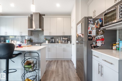Modern kitchen featuring light gray cabinetry, stainless steel appliances, a subway tile backsplash, light wood-finish flooring, and white countertops - 17562 63A Street, Edmonton, AB 