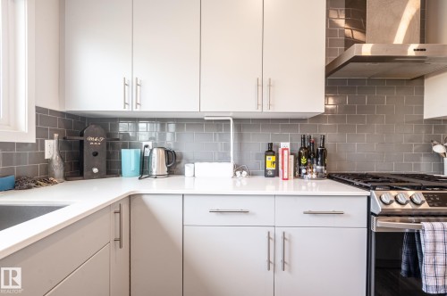 Modern kitchen featuring light gray cabinetry, white countertops, a gray subway tile backsplash, stainless steel range, and a stainless steel range hood - 17562 63A Street, Edmonton, AB 