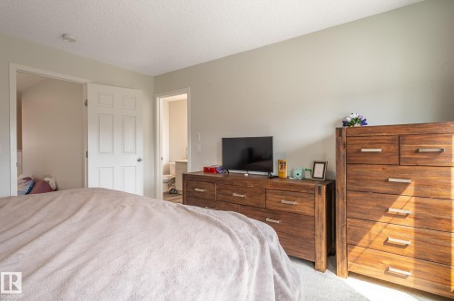 Carpeted bedroom featuring light-colored walls, a textured ceiling, and a paneled interior door - 17562 63A Street, Edmonton, AB 