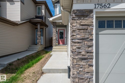 Exterior with stone and siding facade, featuring a red entry door, an attached garage with upper window panels, and a concrete pathway - 17562 63A Street, Edmonton, AB 
