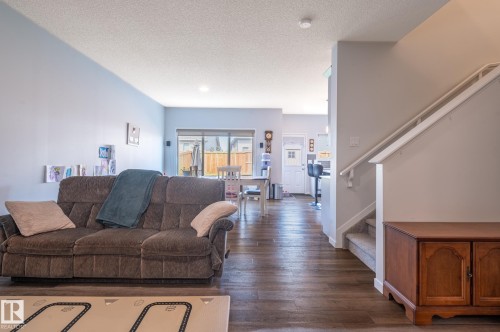 Open-concept living space featuring wood-finish flooring, light-colored walls, and a staircase with carpeted treads - 17562 63A Street, Edmonton, AB 