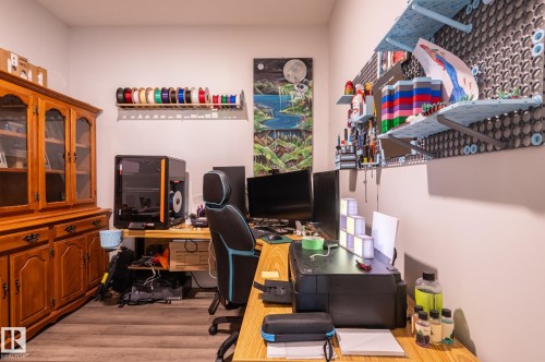 Wood-finish flooring anchors this versatile space, featuring light-toned walls and built-in wall shelving - 17562 63A Street, Edmonton, AB 