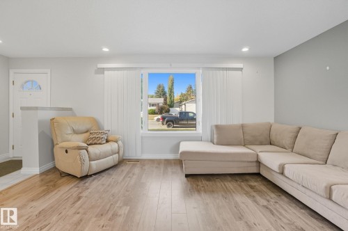 Living space with light wood-finish flooring, recessed lighting, and a large front-facing window with vertical blinds - 14239 53 Street, Edmonton, AB 