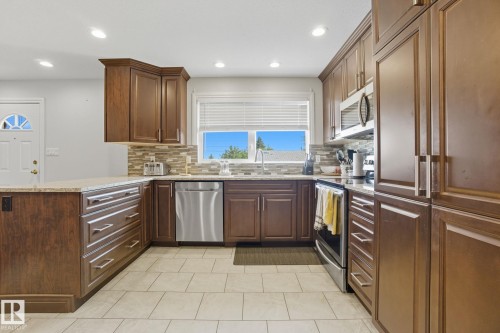Kitchen featuring wood cabinetry, granite-style countertops, stainless steel appliances, tile flooring, and a tiled backsplash - 14239 53 Street, Edmonton, AB 