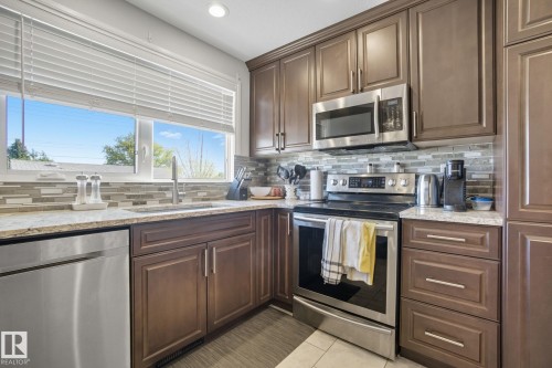 Kitchen featuring brown cabinetry, stainless steel appliances, speckled countertops, and a tiled backsplash - 14239 53 Street, Edmonton, AB 