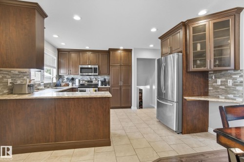 Kitchen featuring wood-finish cabinetry, stainless steel appliances, light-toned countertops, tile flooring, and a mosaic tile backsplash - 14239 53 Street, Edmonton, AB 