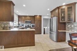 Kitchen featuring wood-finish cabinetry, stainless steel appliances, light-toned countertops, tile flooring, and a mosaic tile backsplash - 