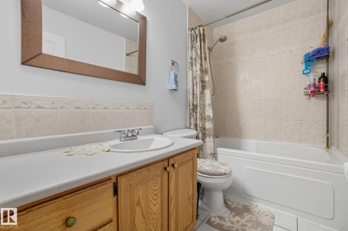 Bathroom featuring a vanity with a white countertop and wood-finish cabinetry, a drop-in sink with a chrome faucet, a framed mirror, and a tiled shower/tub combination - 14239 53 Street, Edmonton, AB 