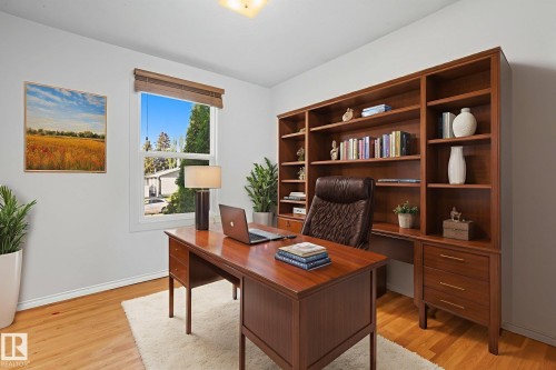 Dedicated space featuring extensive built-in wood shelving and storage, wood-finish flooring, a double-pane window with wood blinds, and crisp white baseboards - 14239 53 Street, Edmonton, AB 