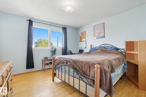 Light-filled room featuring wood-finish flooring, a double window with dark drapery, light blue wall paint, and a ceiling-mounted light fixture - 14239 53 Street, Edmonton, AB 