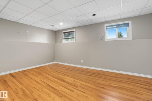 Spacious room featuring wood-finish flooring, light grey walls, white trim, and a grid drop ceiling with recessed lighting - 14239 53 Street, Edmonton, AB 