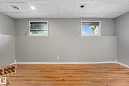 Finished lower-level room featuring wood-finish flooring, two large windows, recessed lighting, and a grid ceiling - 14239 53 Street, Edmonton, AB 