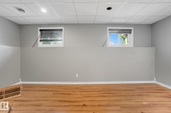 Finished lower-level room featuring wood-finish flooring, two large windows, recessed lighting, and a grid ceiling - 