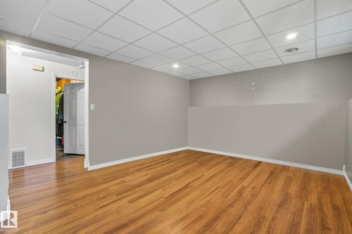 Spacious room featuring wood-finish flooring, light grey walls, white baseboards, and a grid drop ceiling with recessed lighting - 14239 53 Street, Edmonton, AB 