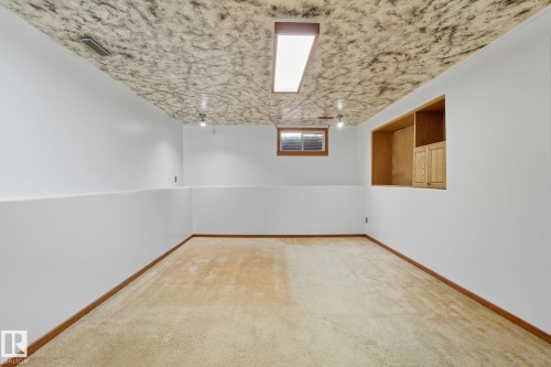 Spacious room featuring light-toned carpeting, white walls with a chair rail, and a patterned ceiling - 14239 53 Street, Edmonton, AB 