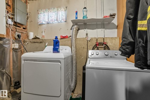Dedicated laundry area featuring a white washing machine and dryer, a window with a valance, and wall-mounted shelving - 14239 53 Street, Edmonton, AB 
