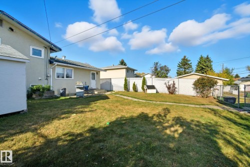 Expansive sloped backyard featuring a manicured lawn, a detached storage shed, a concrete patio, and mature perimeter trees - 14239 53 Street, Edmonton, AB 